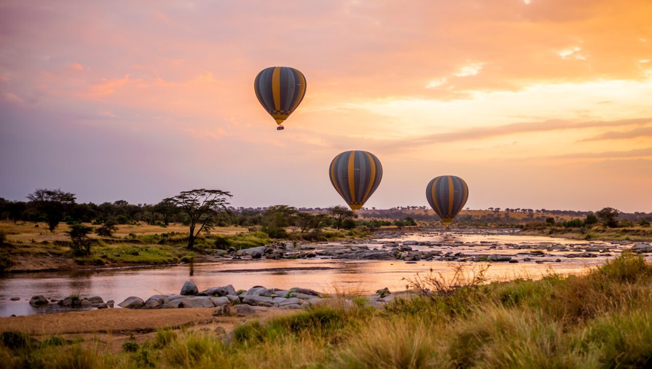 three hot air balloons flying over a river